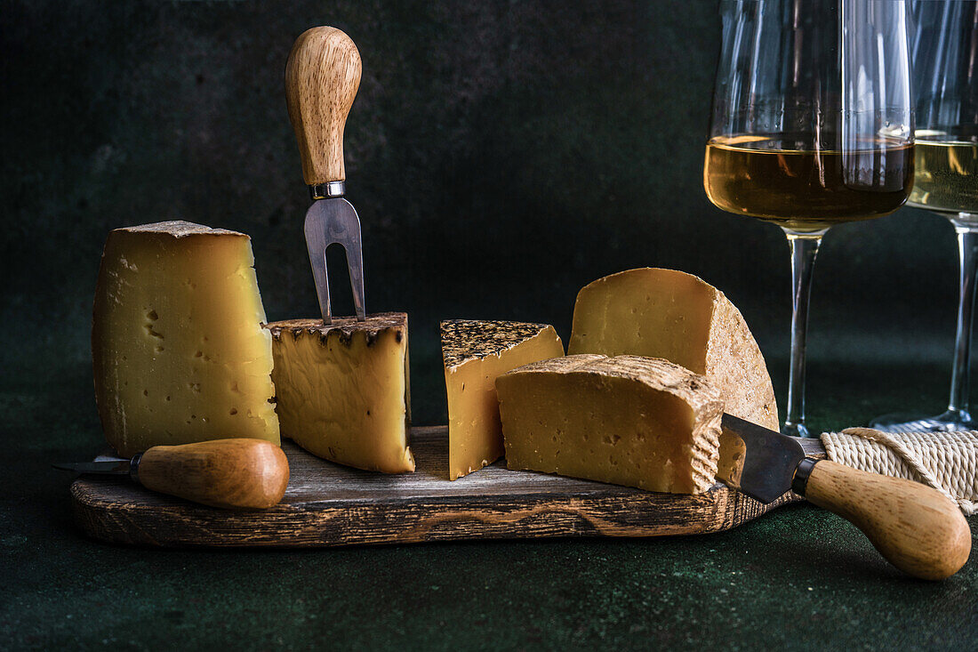 Wooden cutting board with cheese variety on dark concrete background