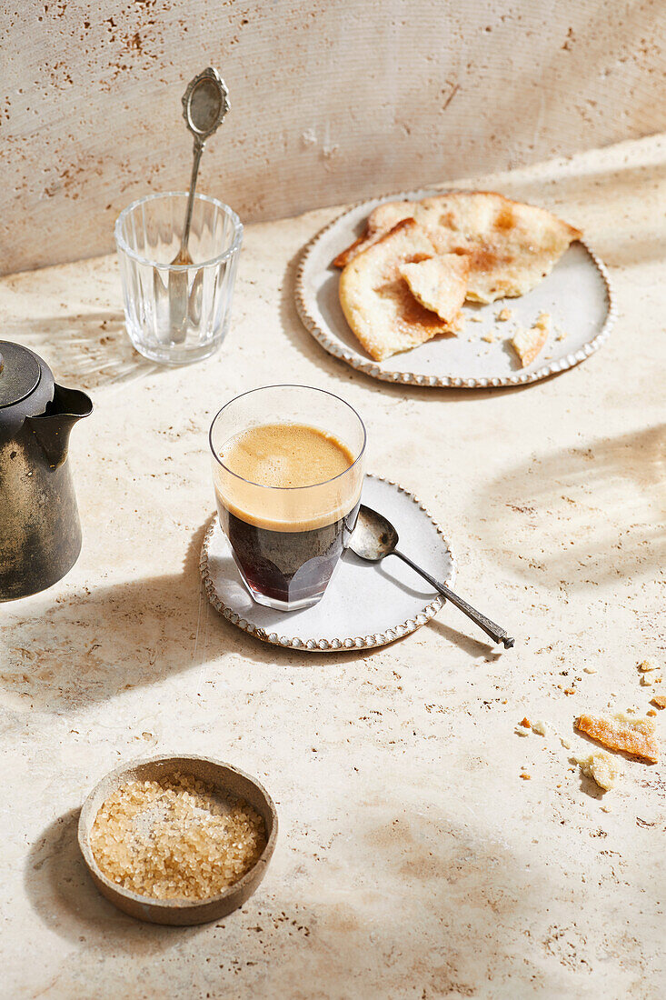 Hoher Blickwinkel auf einen köstlichen heißen Espresso im Glas auf einer Untertasse mit Löffel an einem sonnigen Tag