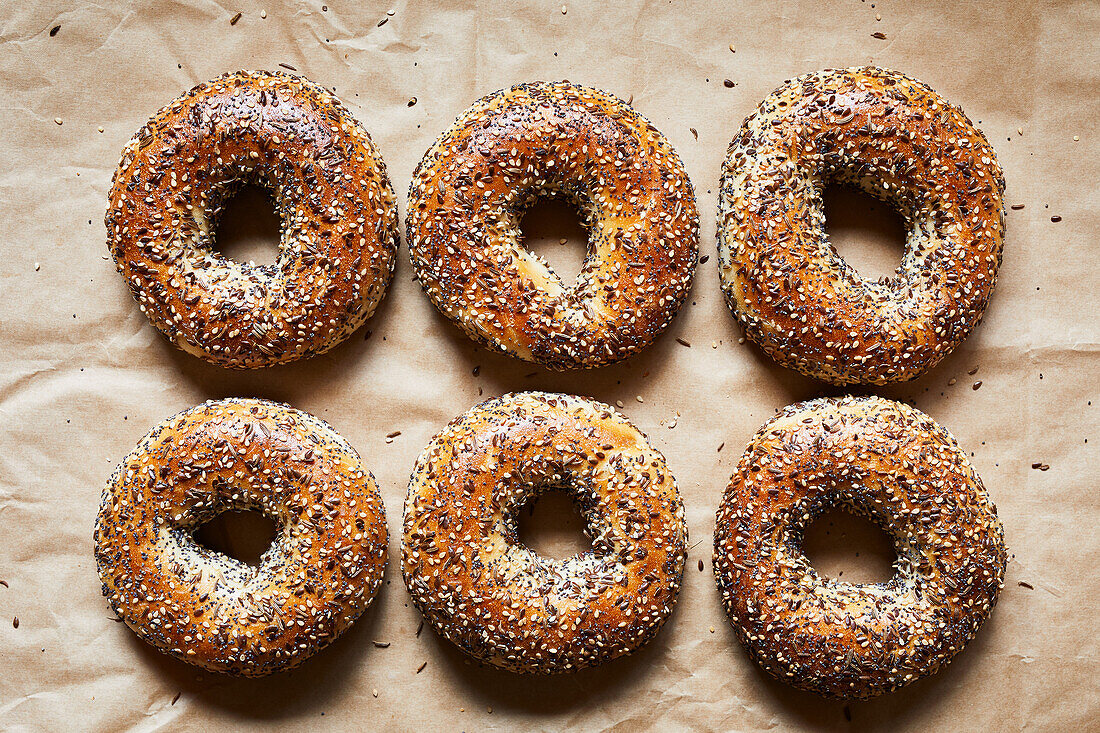 Top view of tasty baked bagels with seeds placed on parchment paper in bakery