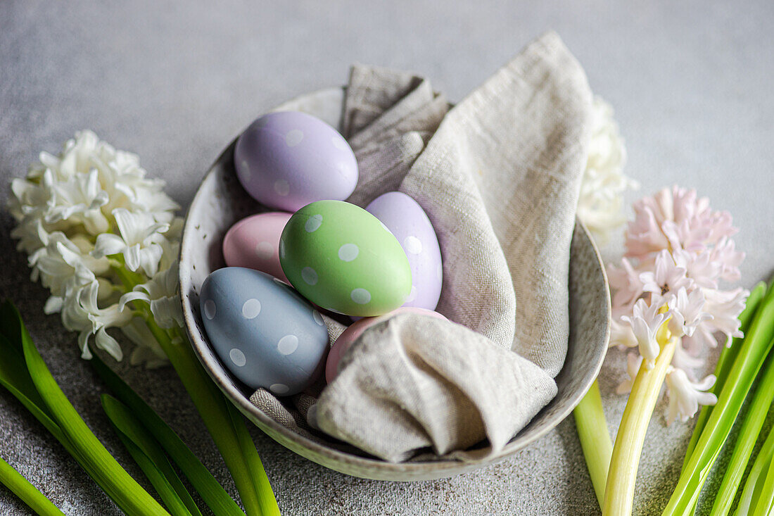 Frühlingshaft gedeckter Tisch mit Hyazinthenblüten und bunten Eiern auf grauem Betontisch für ein festliches Abendessen