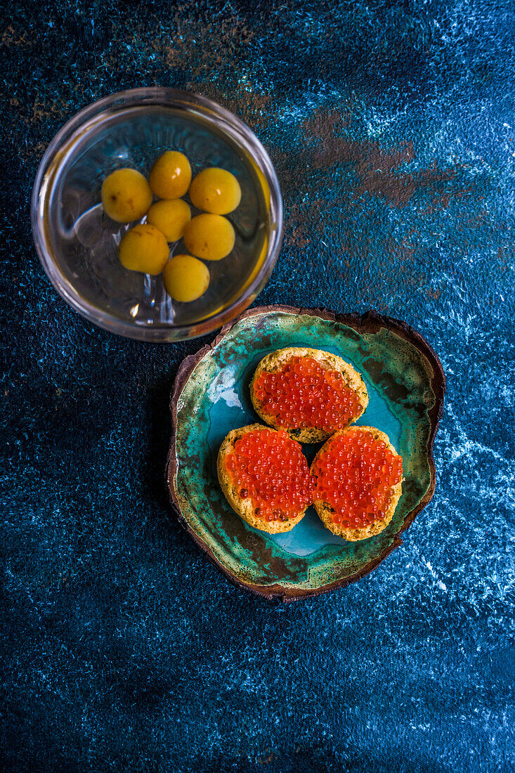 From above bruschetta with red caviar on ceramic plate on stone table near dry martini in glass