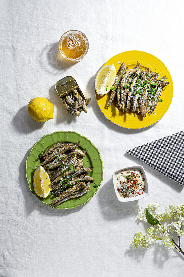 From above of delicious fried anchovies served on plates with lemon and placed on white table with glass of beer