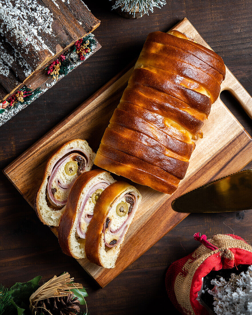 Draufsicht auf köstlichen gebackenen Schinken und Olivenbrot, serviert in einer Bäckerei auf einem Schneidebrett auf dem Tisch