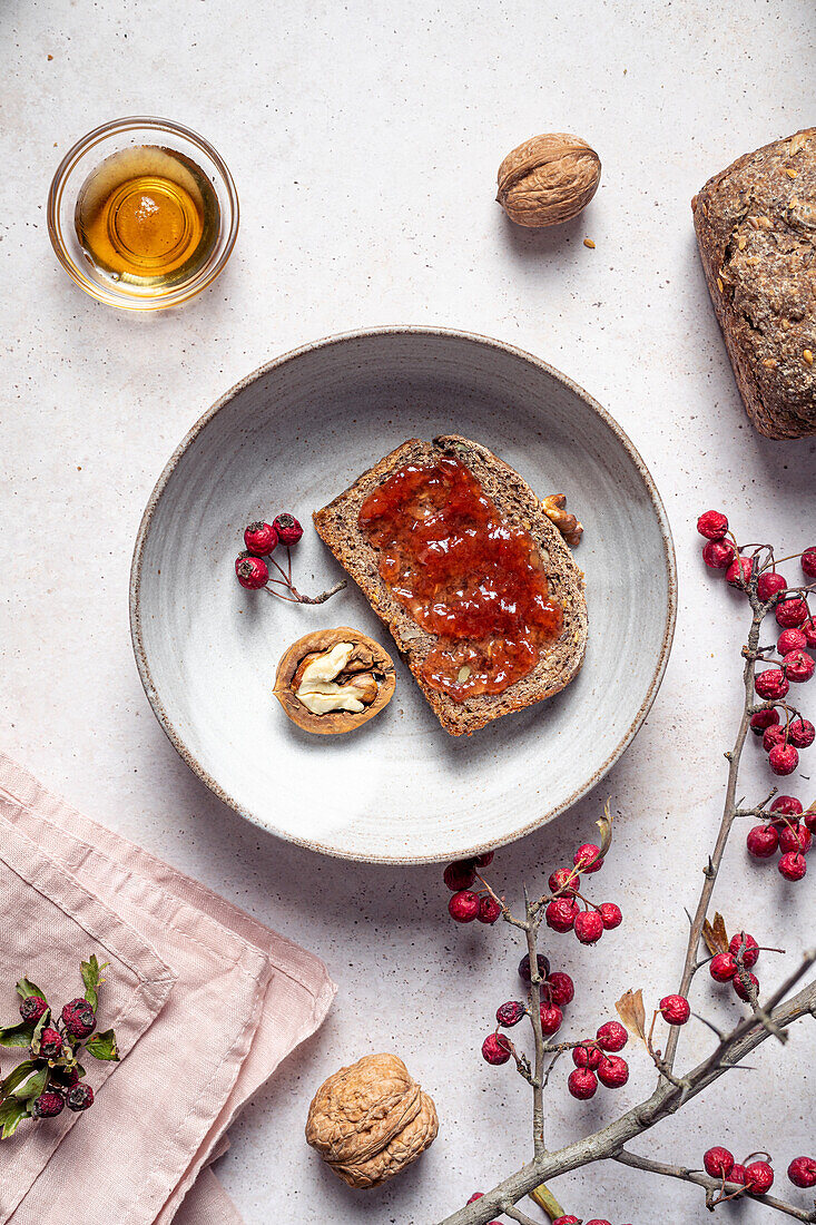 Ansicht von oben von Roggenbrot mit Marmelade neben einer halben Walnuss mit Honig und einem Vogelbeerzweig