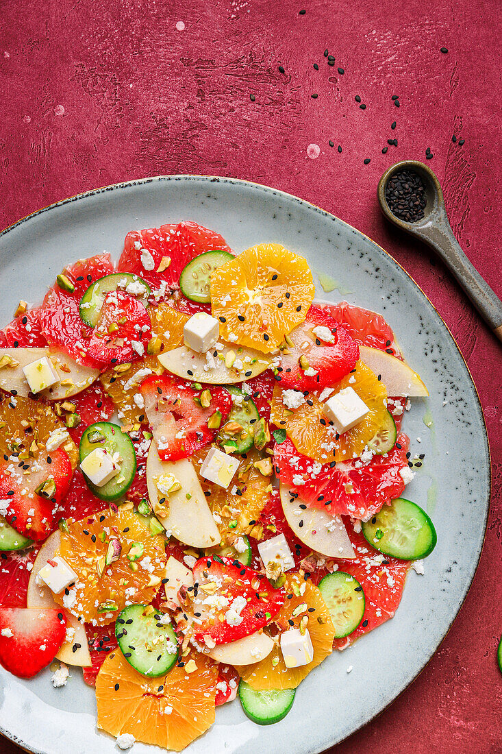 Top view of healthy salad with oranges and strawberries and apples and cucumbers served with cheese and pistachios on plate