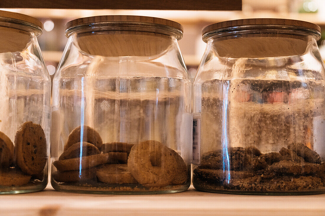 Set of glass jars with chocolate cookies placed on wooden shelf in shop