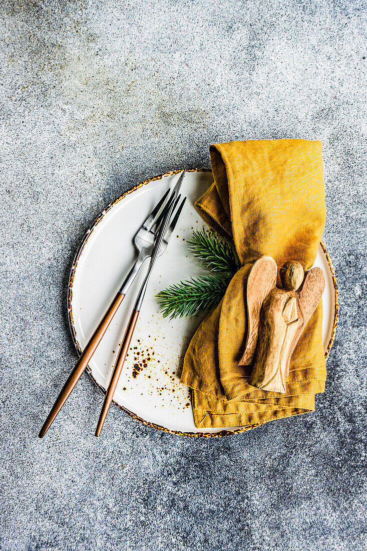 Ceramic plate setting for Christmas dinner with wooden angel ornament on concrete table on grey background