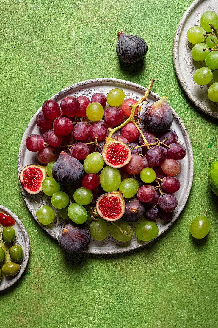 Top view of bunch of delicious fresh juicy red and green grapes served on plate on green background