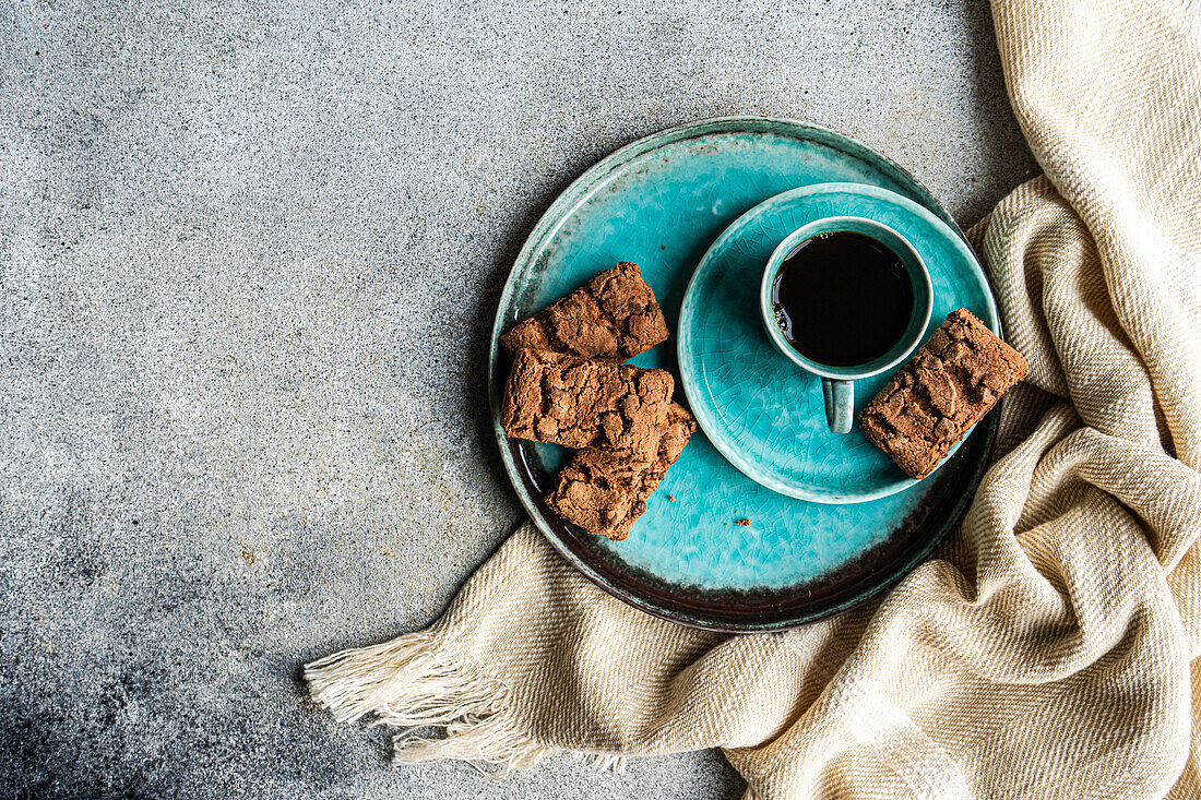 From above ceramic plate with fresh baked chocolate cookies near black coffee drink in a mug on concrete background