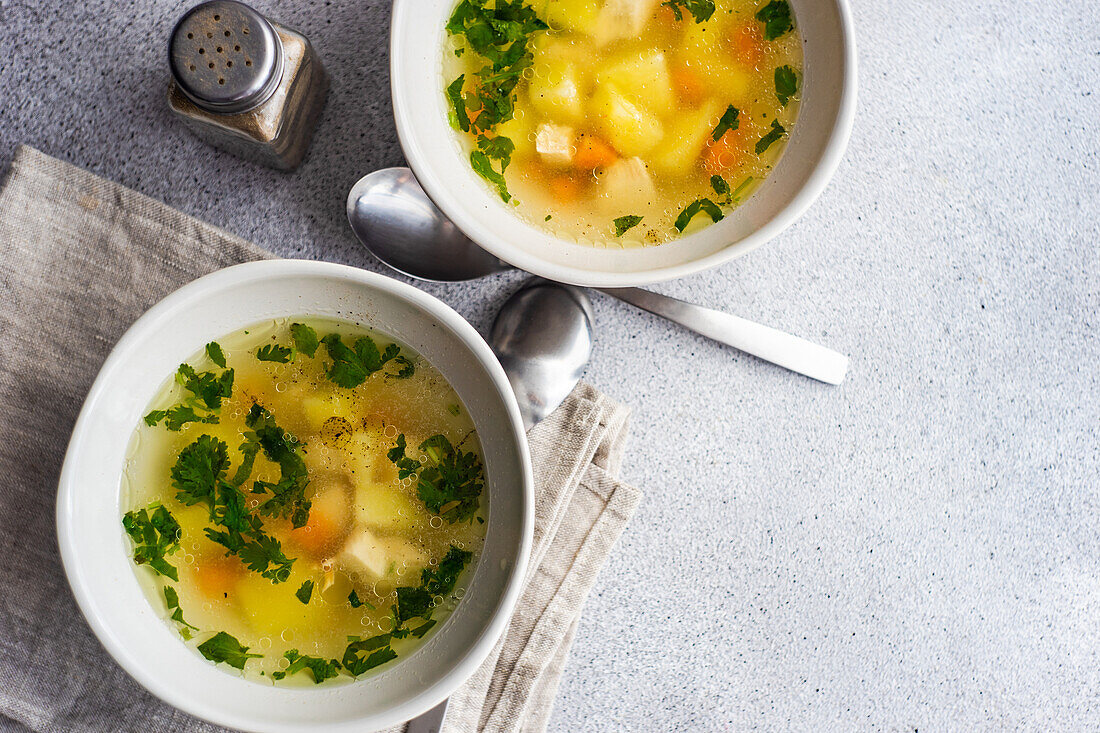 Von oben: Hühnersuppe mit Gemüse in Schalen auf weißem Betontisch, bereit zum Abendessen