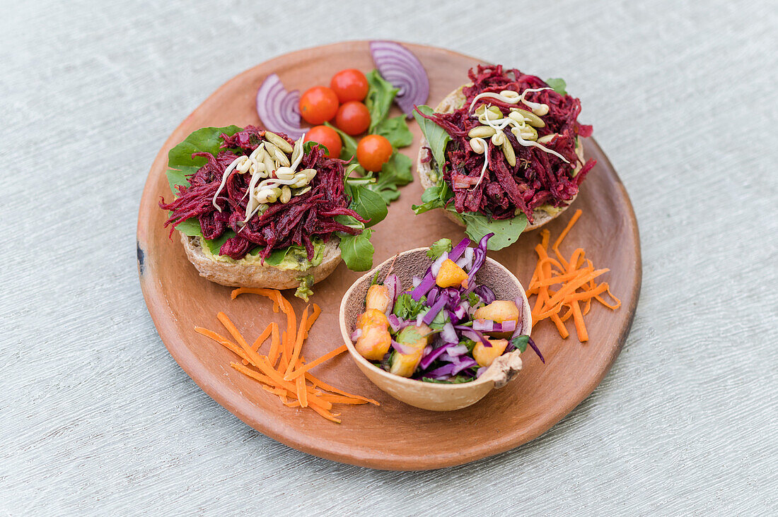 High angle of delicious sandwiches with lettuce and beetroot served with vegetables and fresh salad in bowl on wooden plate on table