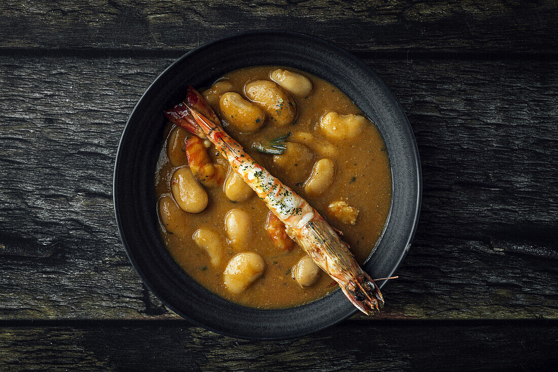 From above of appetizing cream soup with white beans and langoustines served in bowl and placed on wooden tabletop in kitchen