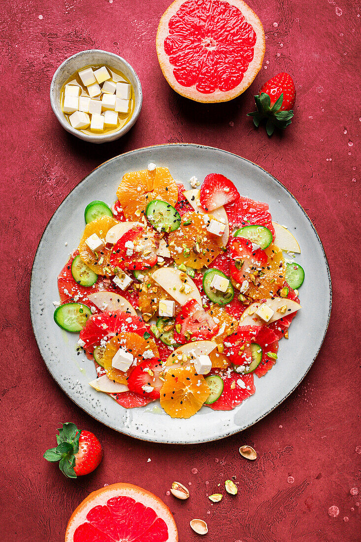 Top view of healthy salad with oranges and strawberries and apples and cucumbers served with cheese and pistachios on plate