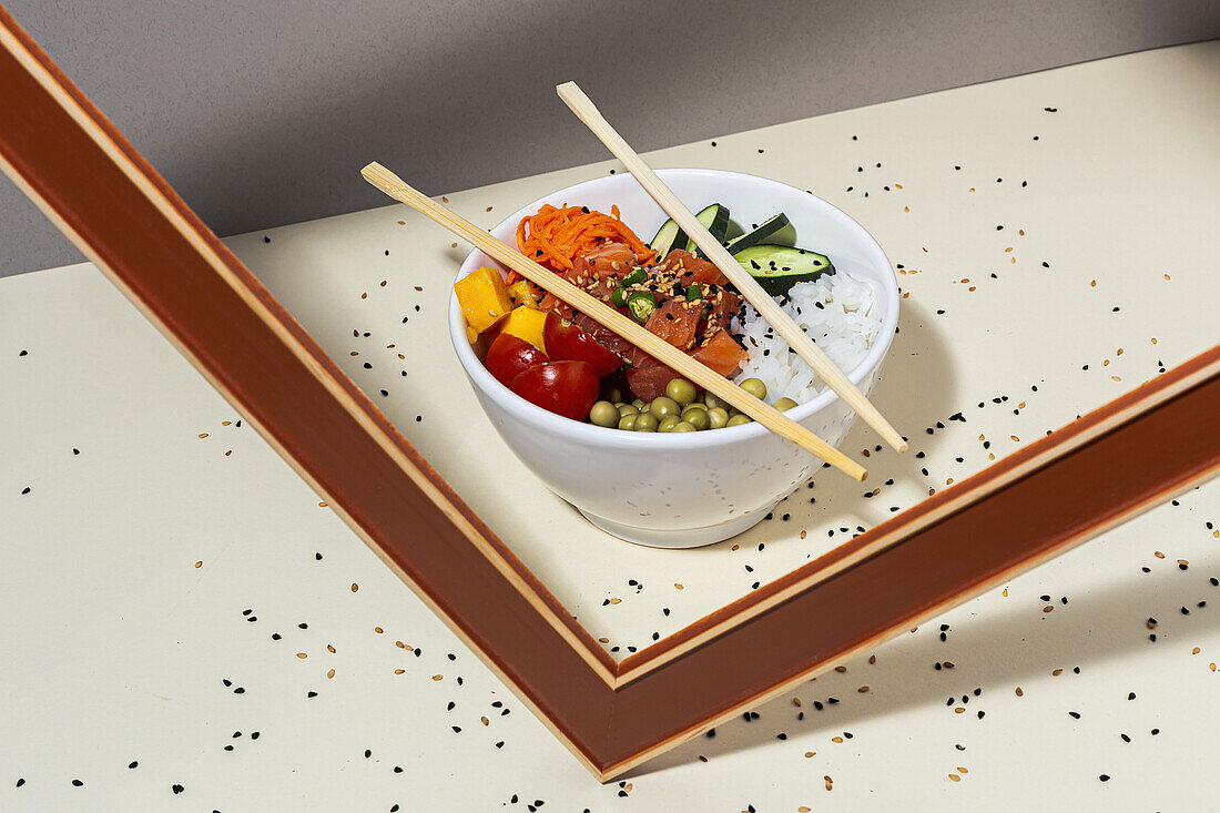 White bowl with tasty poke dish and chopsticks placed behind frame on table covered with sesame seeds