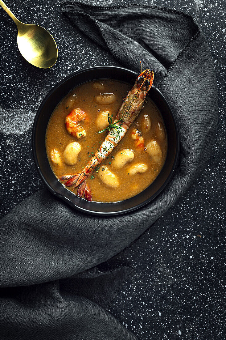 From above of appetizing cream soup with white beans and langoustines served in bowl and placed on marble tabletop near napkin in kitchen