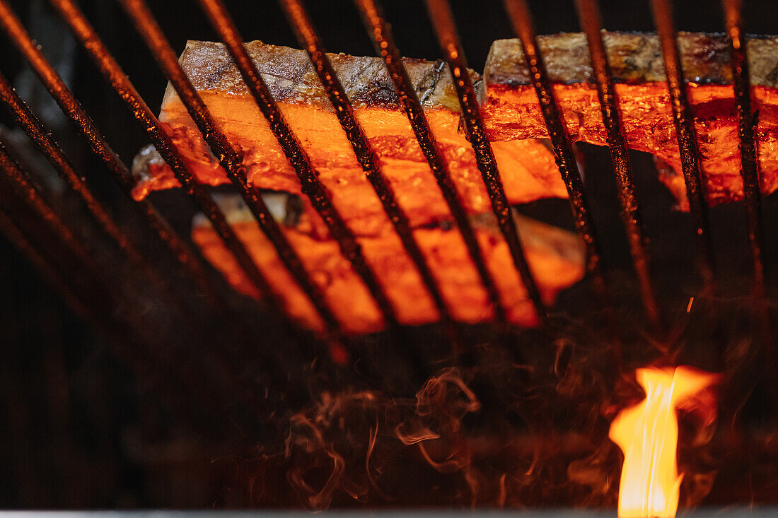 Appetitliche saftige Steaks auf einem Grillrost über einer brennenden Flamme beim Braten im Grillofen