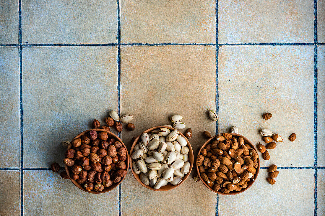 From above row of bowls with different kinds of nuts on concrete tiled table background