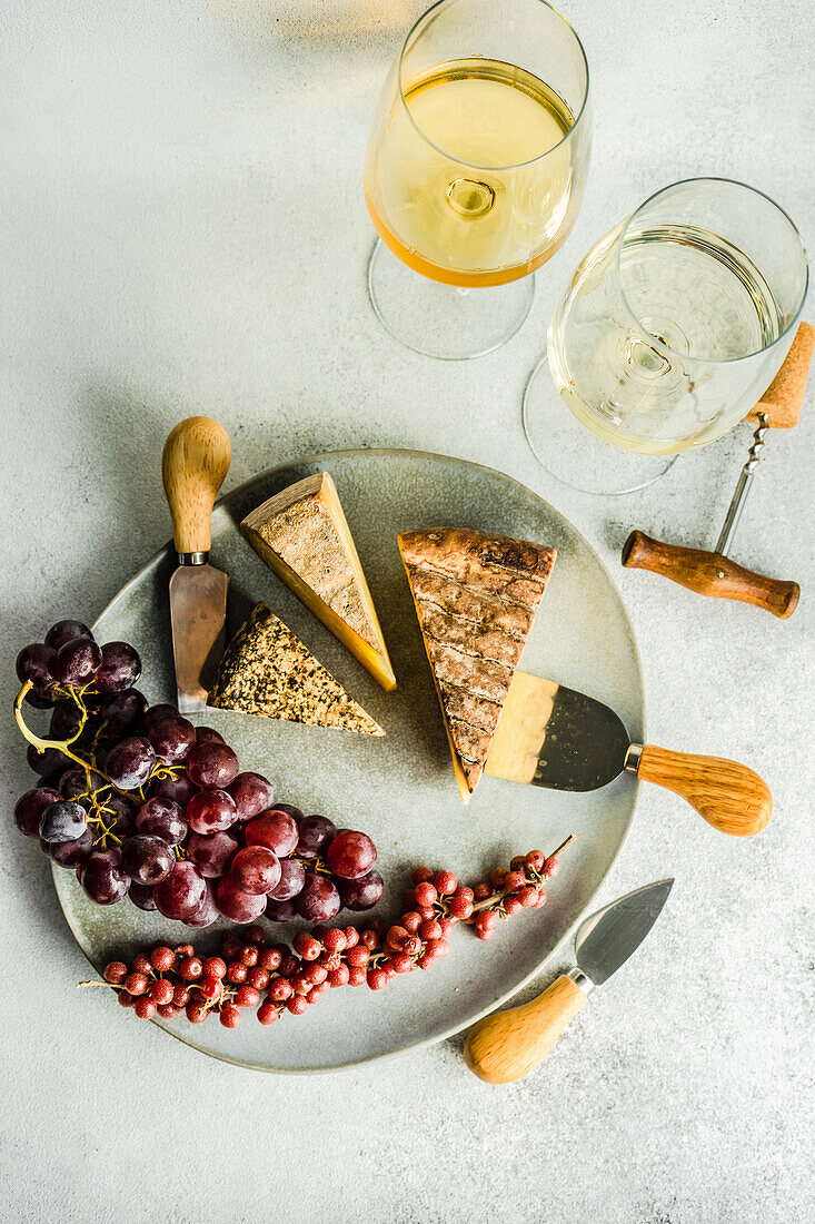 Von oben Käsevariation mit frischen Früchten auf der Steinplatte und Weißwein im Glas auf dem Betontisch