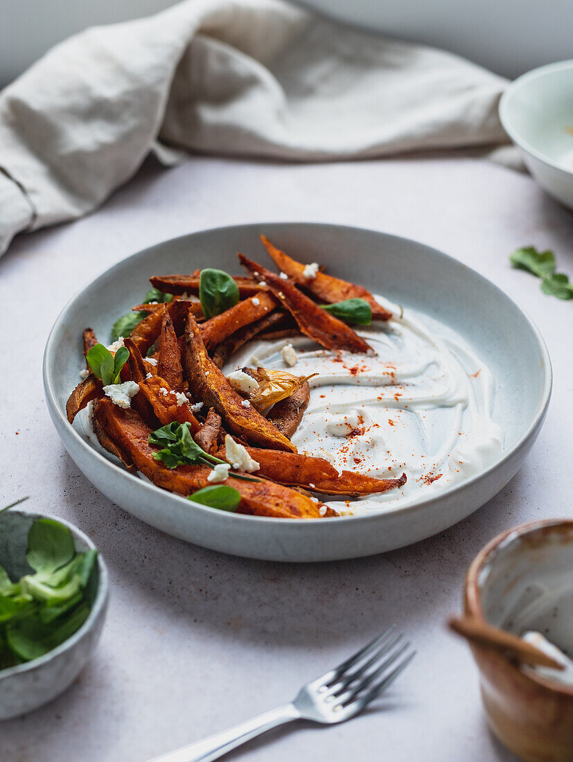 High angle of delicious sweet potato fries with sour cream and herbs served on table