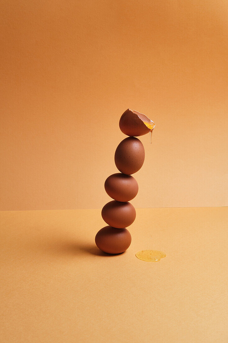 Stack of brown fresh eggs balancing on table on peach background in studio