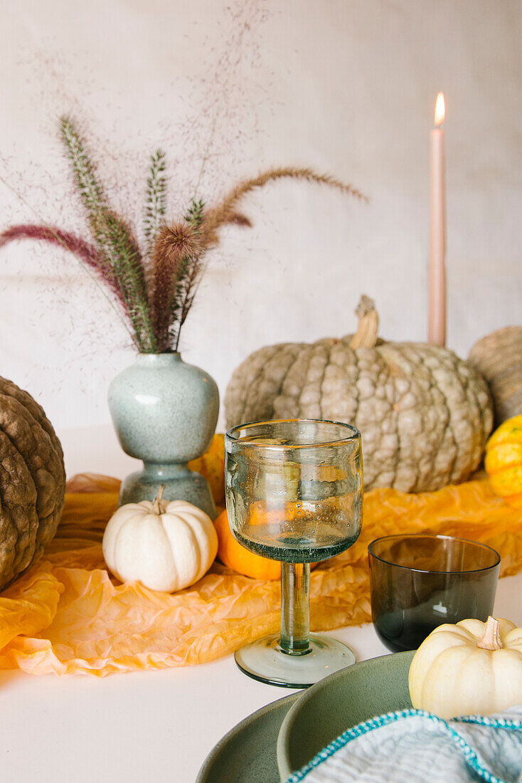 Creative table setting with assorted pumpkins compose with burning candles and vases with dry plants placed near ceramic plate and glasses during Halloween dinner