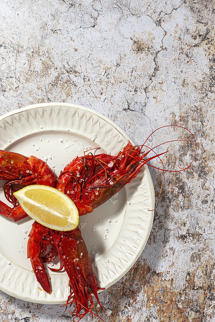 Tasty seafood of cooked red shrimps with fresh lemon slices and coarse salt on white background