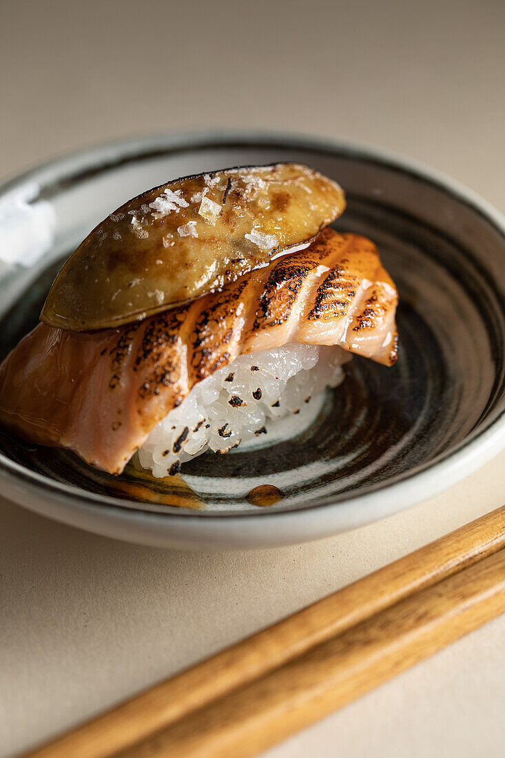 Von oben schmackhafte japanische Nigiri-Sushi mit geräuchertem Lachs und flambierter Gänsestopfleber, serviert auf einem Teller mit Stäbchen in einem Restaurant