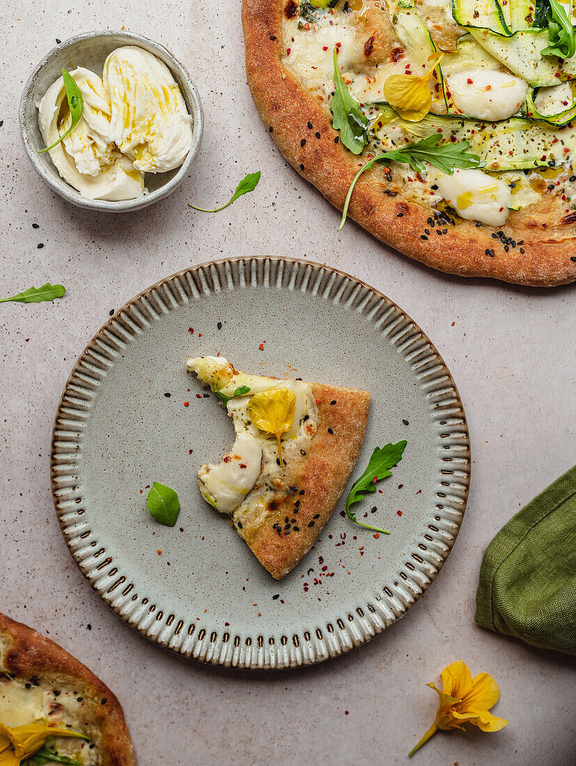 Overhead view of appetizing slice of pizza with arugula leaves and squash flower on melted cheese on gray background