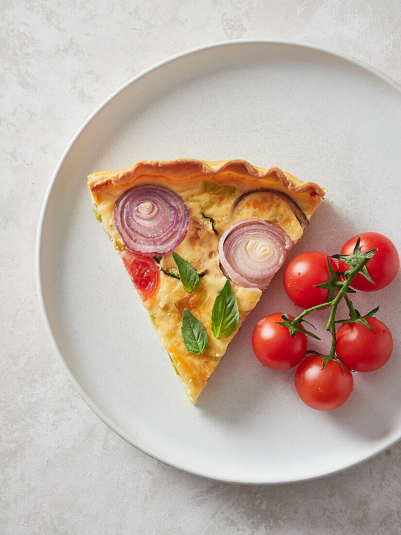 Top view of piece of delicious quiche and bunch of cherry tomatoes served for lunch on plate