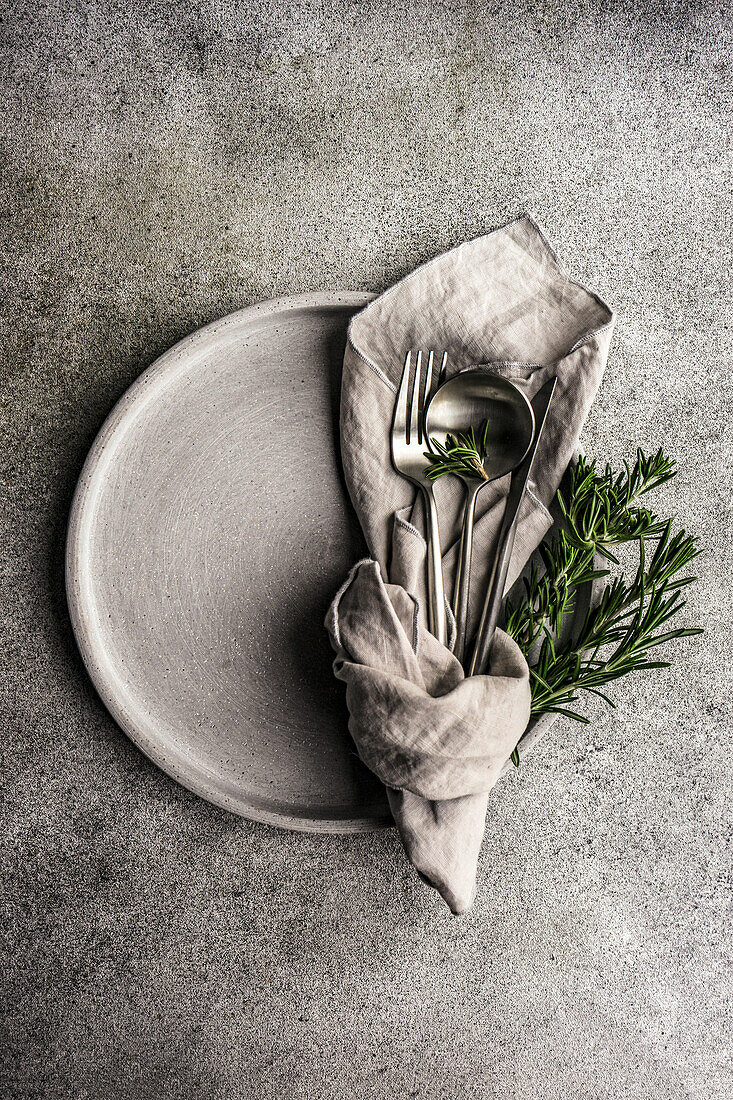 Dinner set with plate and cutlery decorated with fresh rosemary herb
