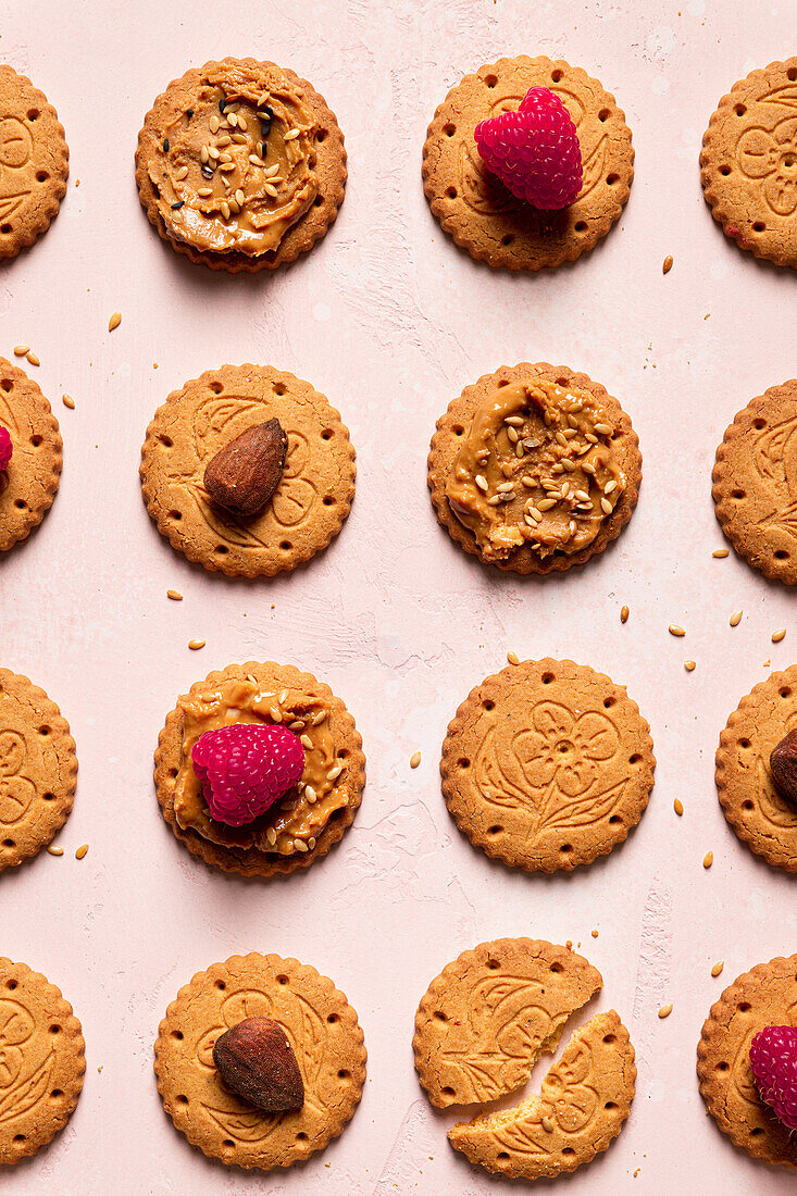 Draufsicht auf appetitliche knusprige Kekse mit Erdnussbutter mit Sesam, Himbeeren und Nüssen auf einem Tisch als abstrakter Hintergrund