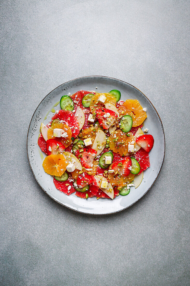 Top view of healthy salad with oranges and strawberries and apples and cucumbers served with cheese and pistachios on plate