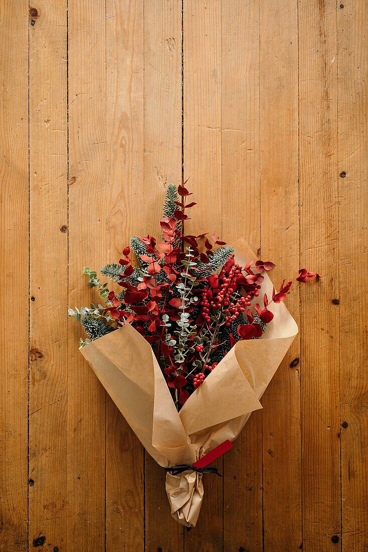 Festlicher, stilvoller, dekorativer Weihnachtsstrauß mit Eukalyptuszweigen und leuchtend roten Zweigen mit Beeren auf einem Holztisch mit Kerzen im Raum von oben