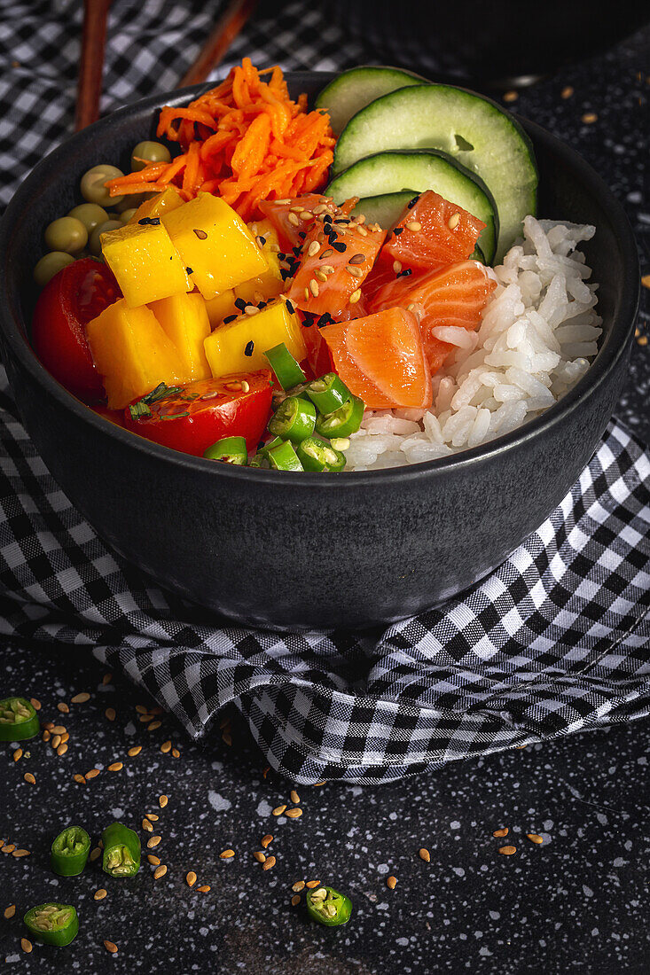 Asiatischer Poke mit Lachs und Reis mit verschiedenen Gemüsesorten, serviert in einer Schüssel auf einem Tisch mit Stäbchen in einem Restaurant