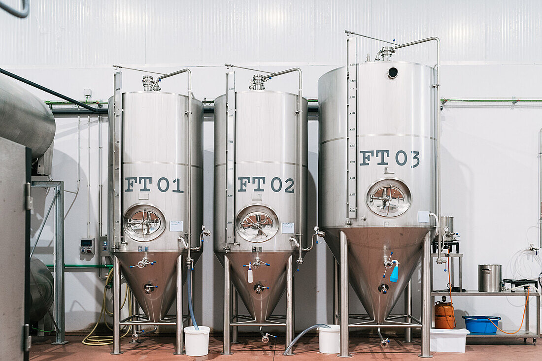 Stainless steel mash boiler near lauter tun with hoses on floor in light brewing company