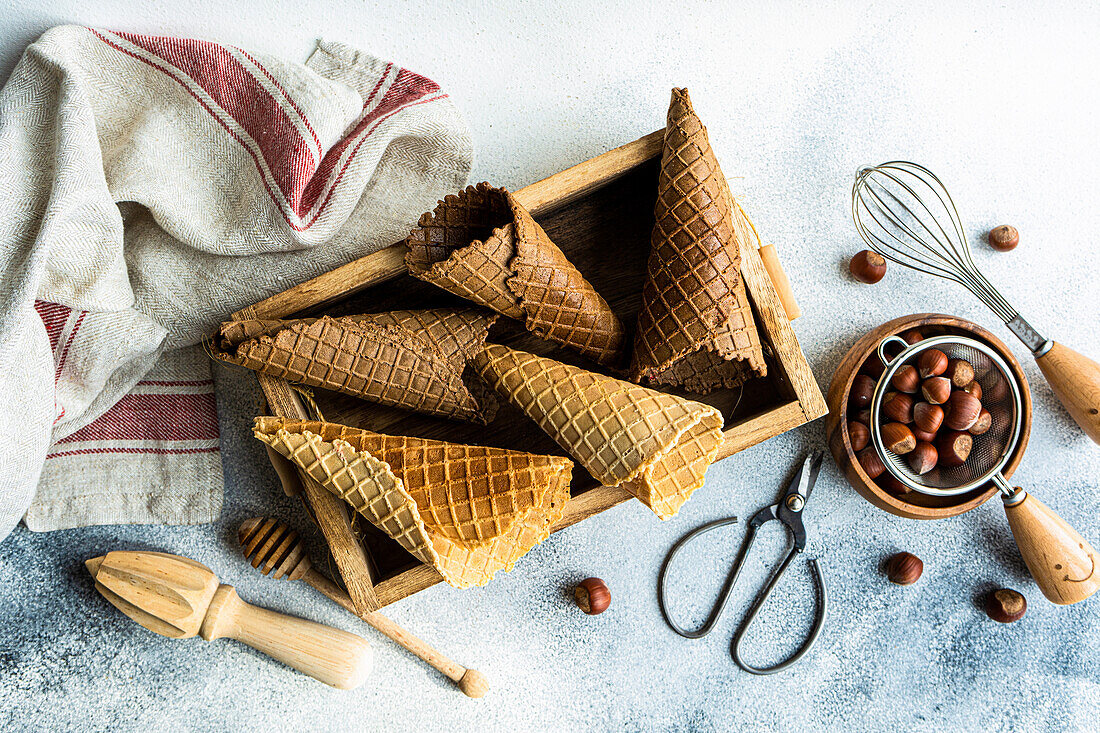 Wooden box with empty waffle cones, bowl with hazelnuts and tools for ice cream cooking