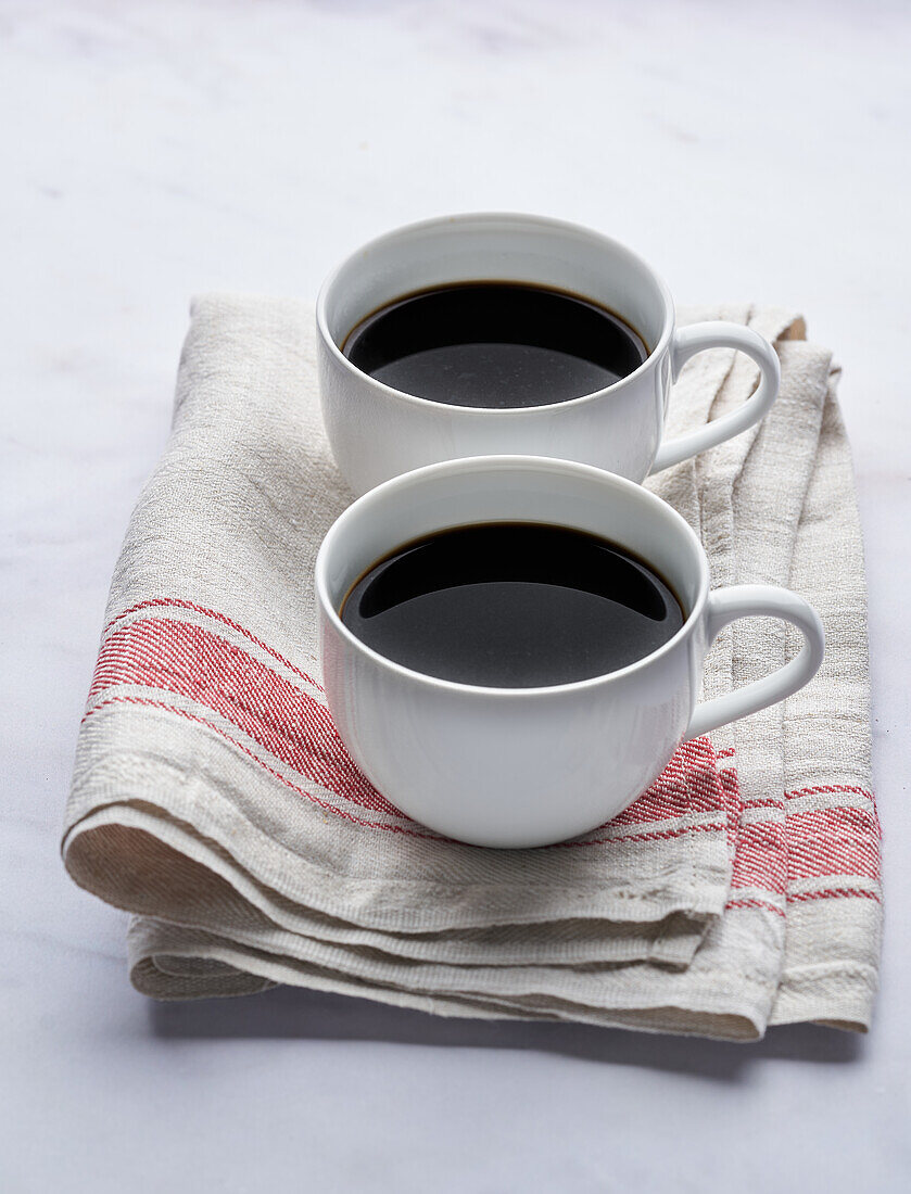 Von oben gesehen zwei aromatische Kaffeetassen auf einer Serviette auf einem weißen Marmortisch an einem sonnigen Morgen