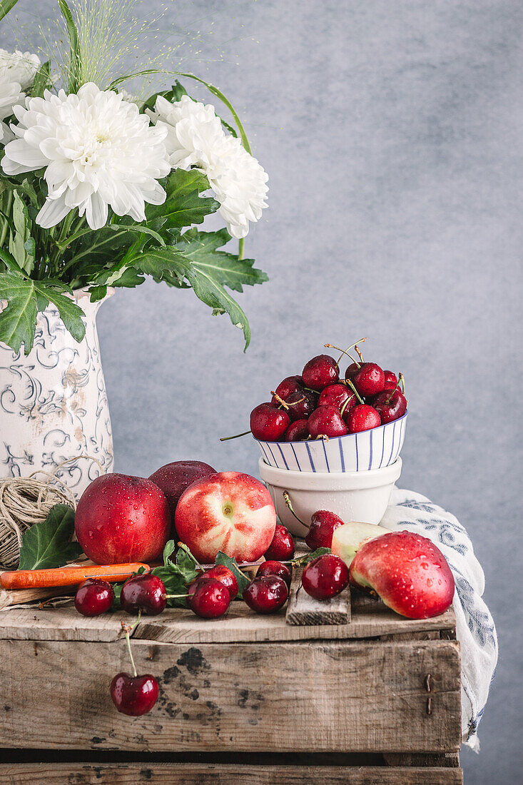 Stilleben mit reifen Nektarinen und Kirschen auf einem rustikalen Tisch mit Blumen in einer Vase auf grauem Hintergrund im Studio