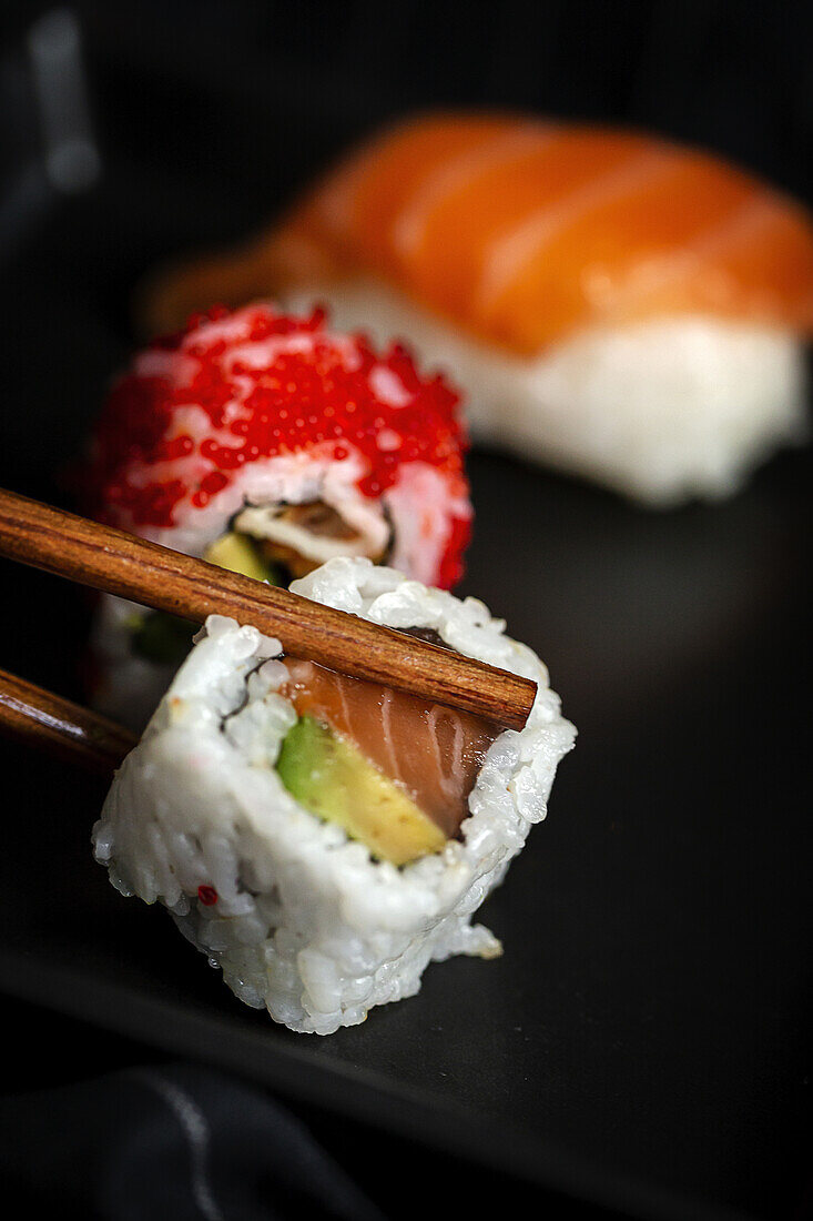 Top view composition of delicious fresh various sushi and bamboo chopsticks served on black platter on checkered cloth