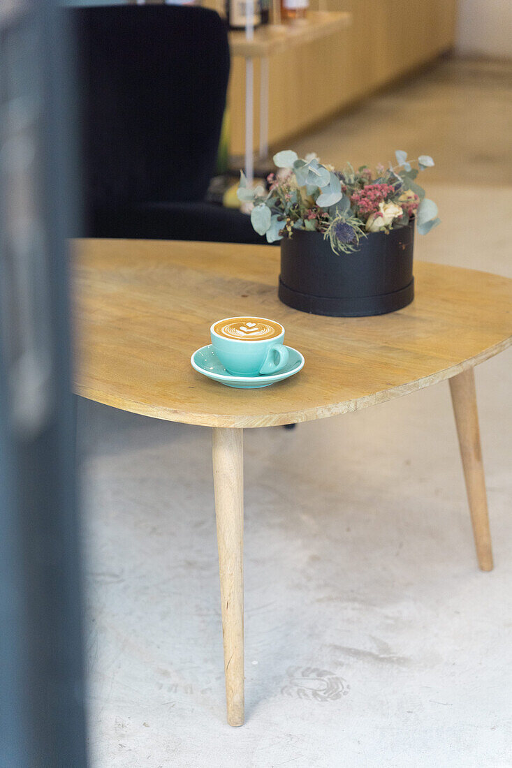 Mug of hot coffee with creative latte art served on plate with teaspoon on wooden table in modern light coffee house