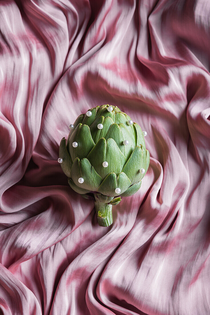 Top view of green artichoke with small beads on crumpled silk fabric