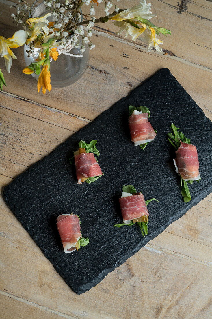 Top view of stuffed tuna rolls served on black board near bouquet of blooming flowers in vase