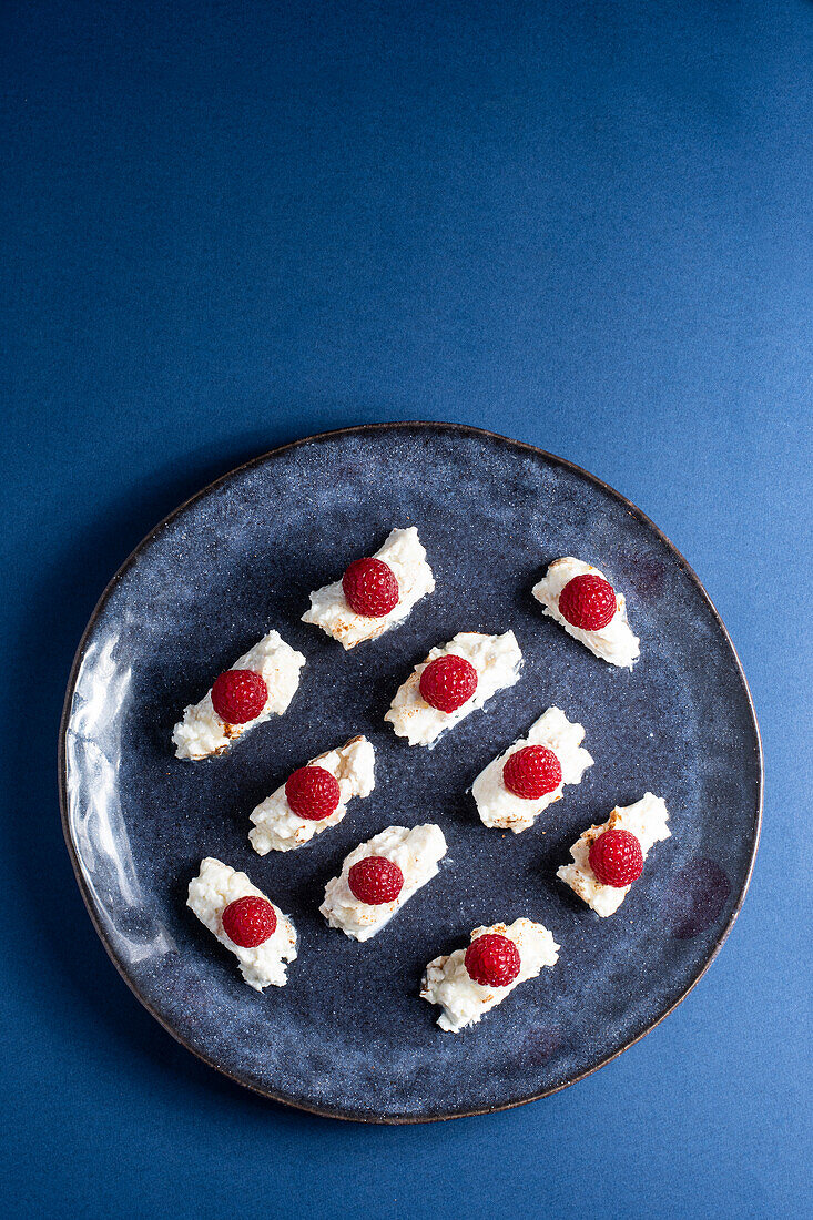 Draufsicht auf ein appetitliches hausgemachtes Dessert mit Sahne und Himbeeren auf einem Teller vor blauem Hintergrund