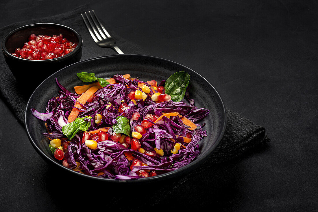 Homemade Purple Cabbage Salad with Corn, Carrots, Pomegranate and Spinach on dark background. Vegan food concept. Healthy food