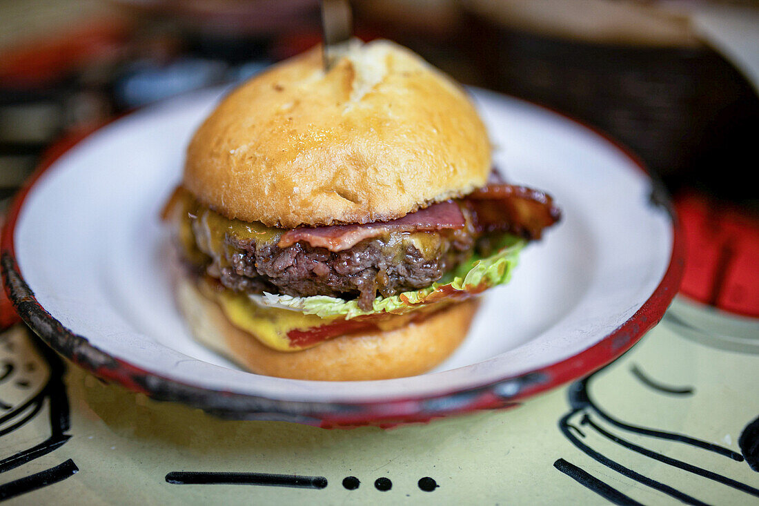 Leckerer Burger mit Fleisch, Speck und Salat, serviert auf einem Teller mit Messer im Restaurant