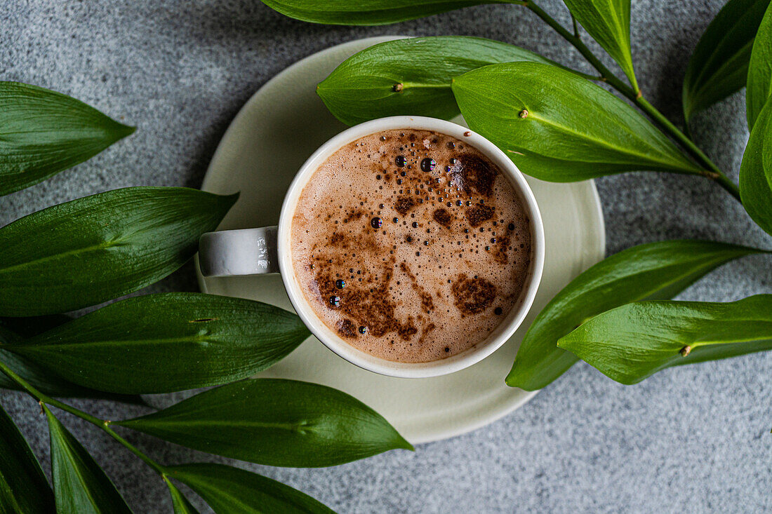 Tasse Cappuccino und grüne Blätter der Ruscus-Pflanze