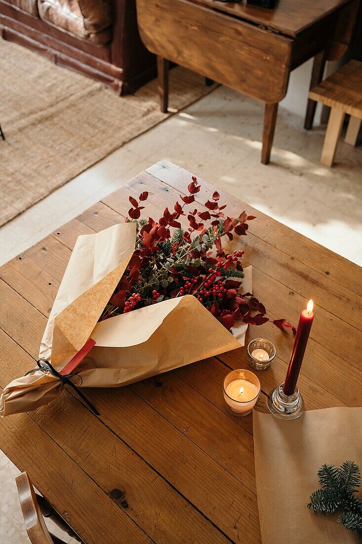 Festlicher, stilvoller, dekorativer Weihnachtsstrauß mit Eukalyptuszweigen und leuchtend roten Zweigen mit Beeren auf einem Holztisch mit Kerzen im Raum von oben