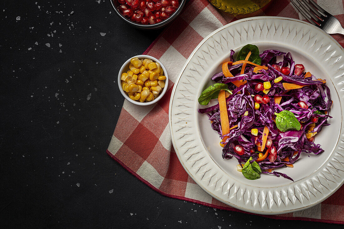 Homemade Purple Cabbage Salad with Corn, Carrots, Pomegranate and Spinach on dark background. Vegan food concept. Healthy food