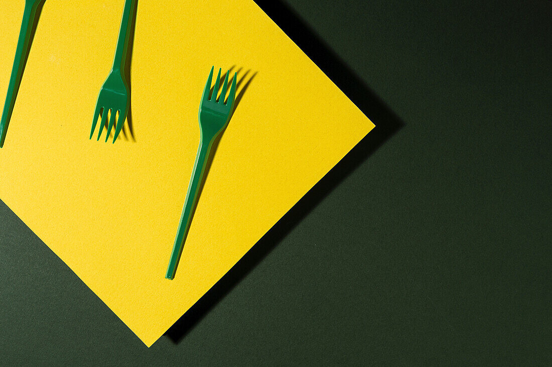 Overhead view of bright green eco friendly fork near yellow carton sheet on green background