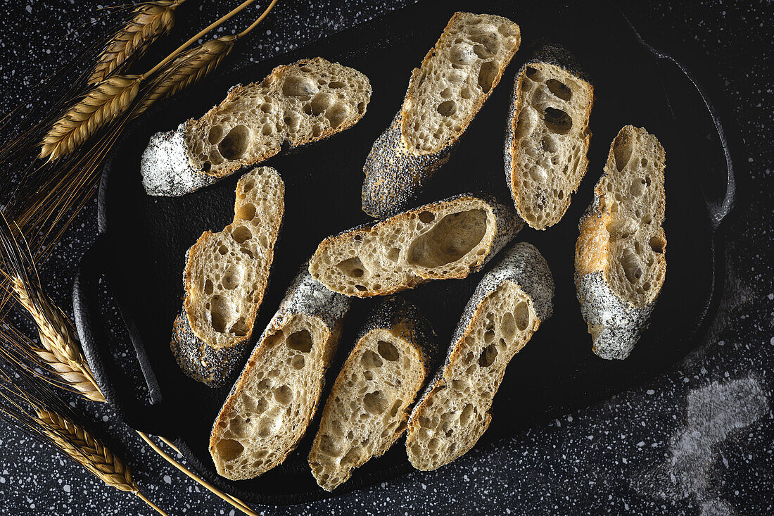 Von oben appetitliches knuspriges Brot in der Nähe von Weizenspitzen und dunklem Stoff auf dem Tisch